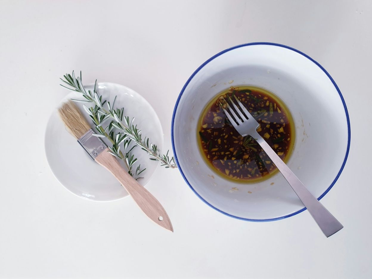 A bowl of marinade and a sprig of rosemary