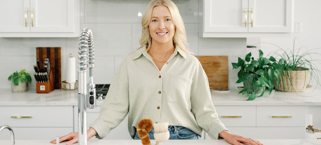 Women standing in a light and airy kitchen with a green shirt and eco-friendly products