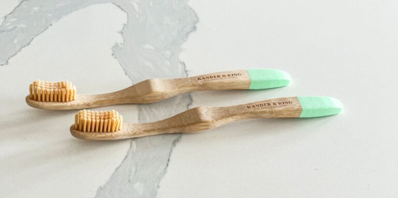 Two Bamboo toothbrushes with green tips laying on a quartz counter