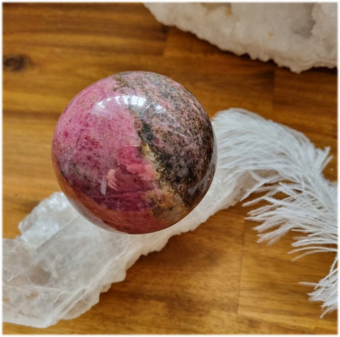 Rhodonite sphere on a piece of gypsum next to a feather