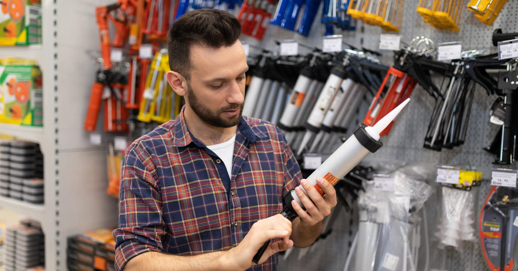 a man in a hardware store chooses a caulk gun