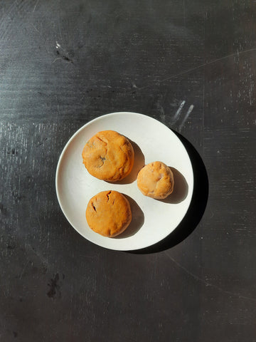 Mooncake tests. The mooncakes look like biscuits because they are not shaped. Three mooncakes are on a white plate. The plate is on a black table.