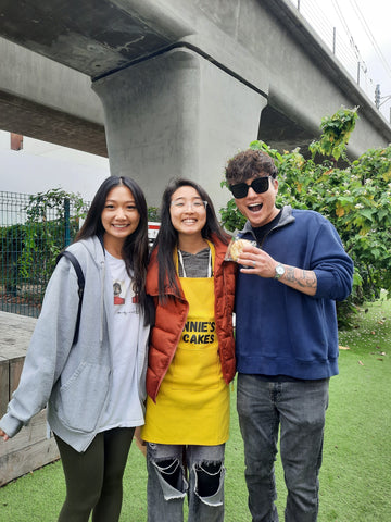 Annie wearing a yellow Annie's T Cakes apron. Annie is standing between two TikTok and Instagram influencers Andy (right) and Michelle (left). The image was taken at Maum Market in Los Angeles.