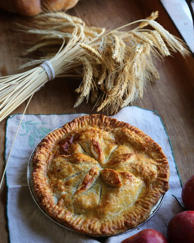 A pie with wheat above it on a table. 