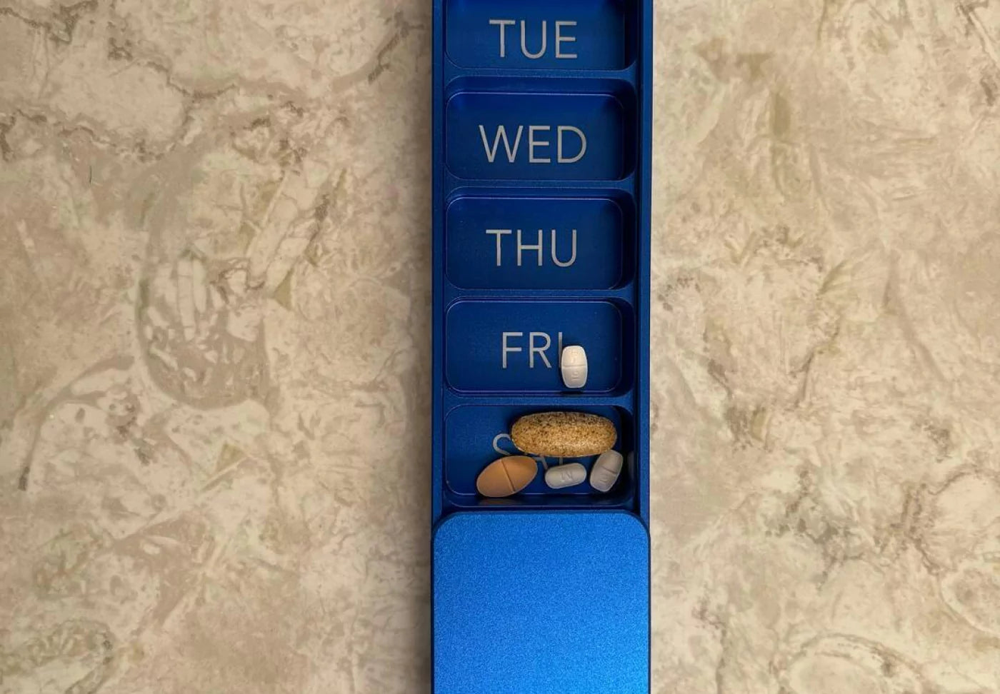 A weekly pill organizer with compartments for Tuesday to Friday, containing various pills.