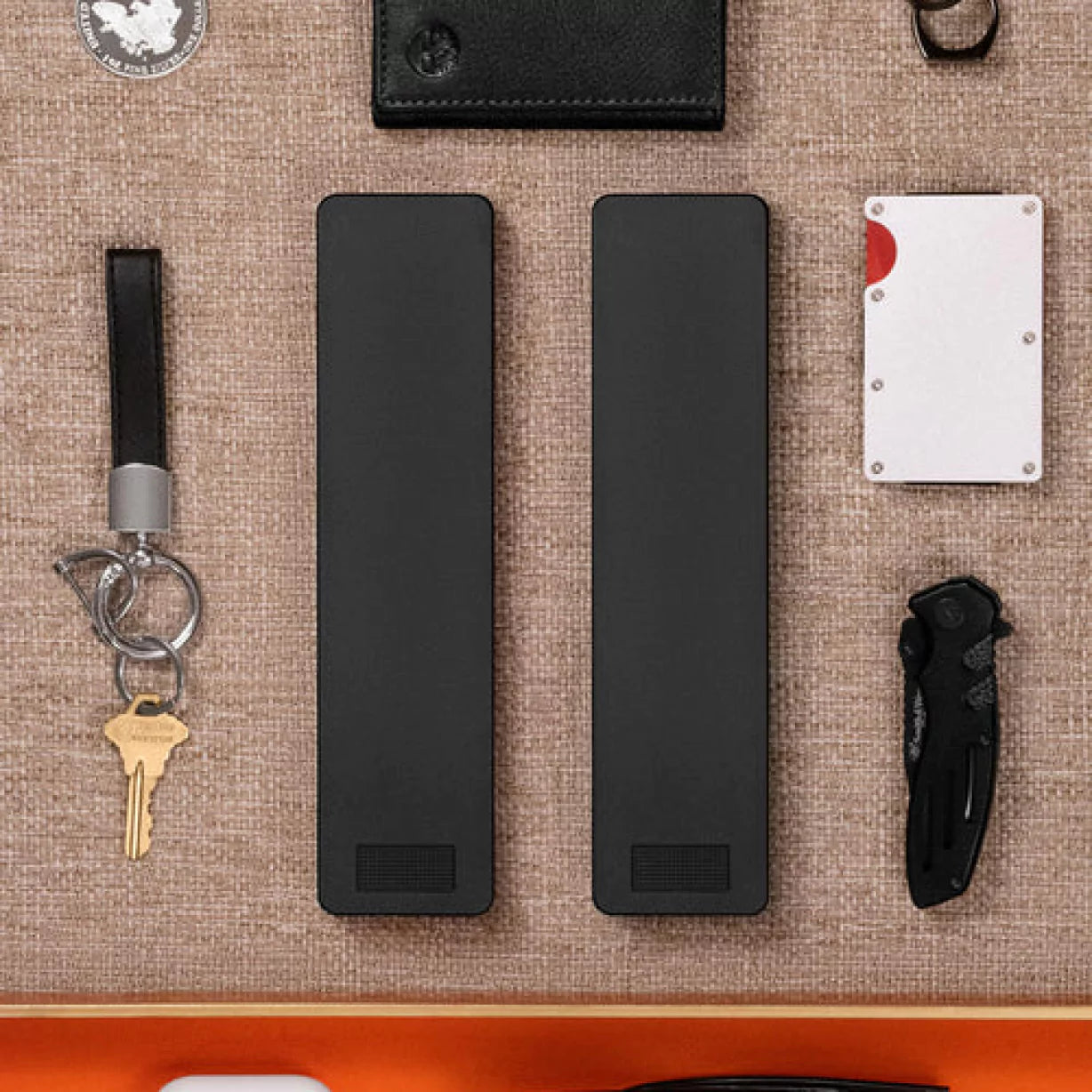 Elegantly organized everyday carry items, including two slim devices, a key, wallet, and a folding knife.