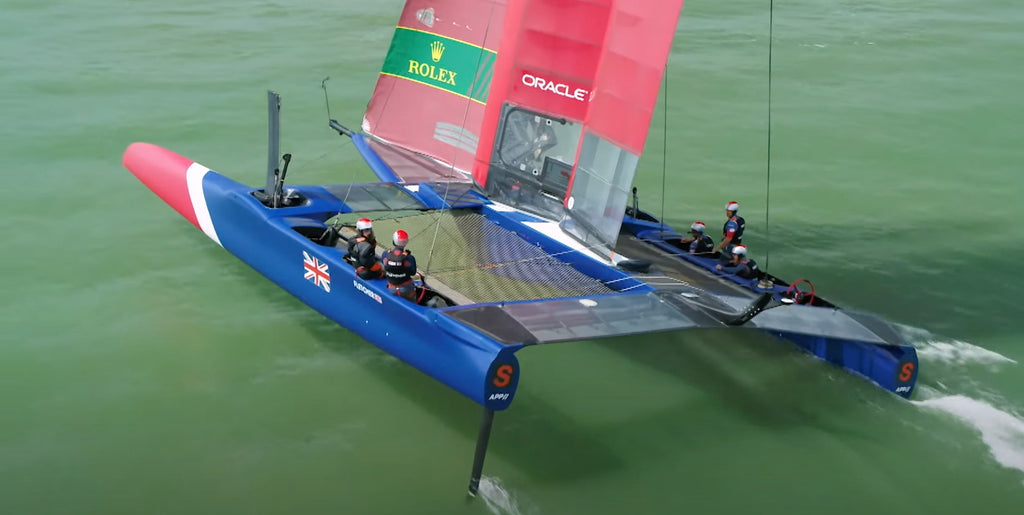 The British SailGP team F50 Catamaran sailing on foils - blue and red hull, red sails and green sea