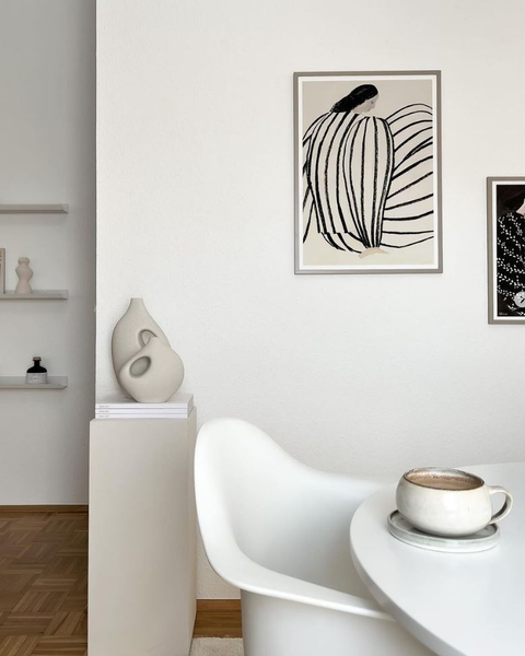 Fehér fal előtt fehér asztal és szék, a falon fekete dekor képpel