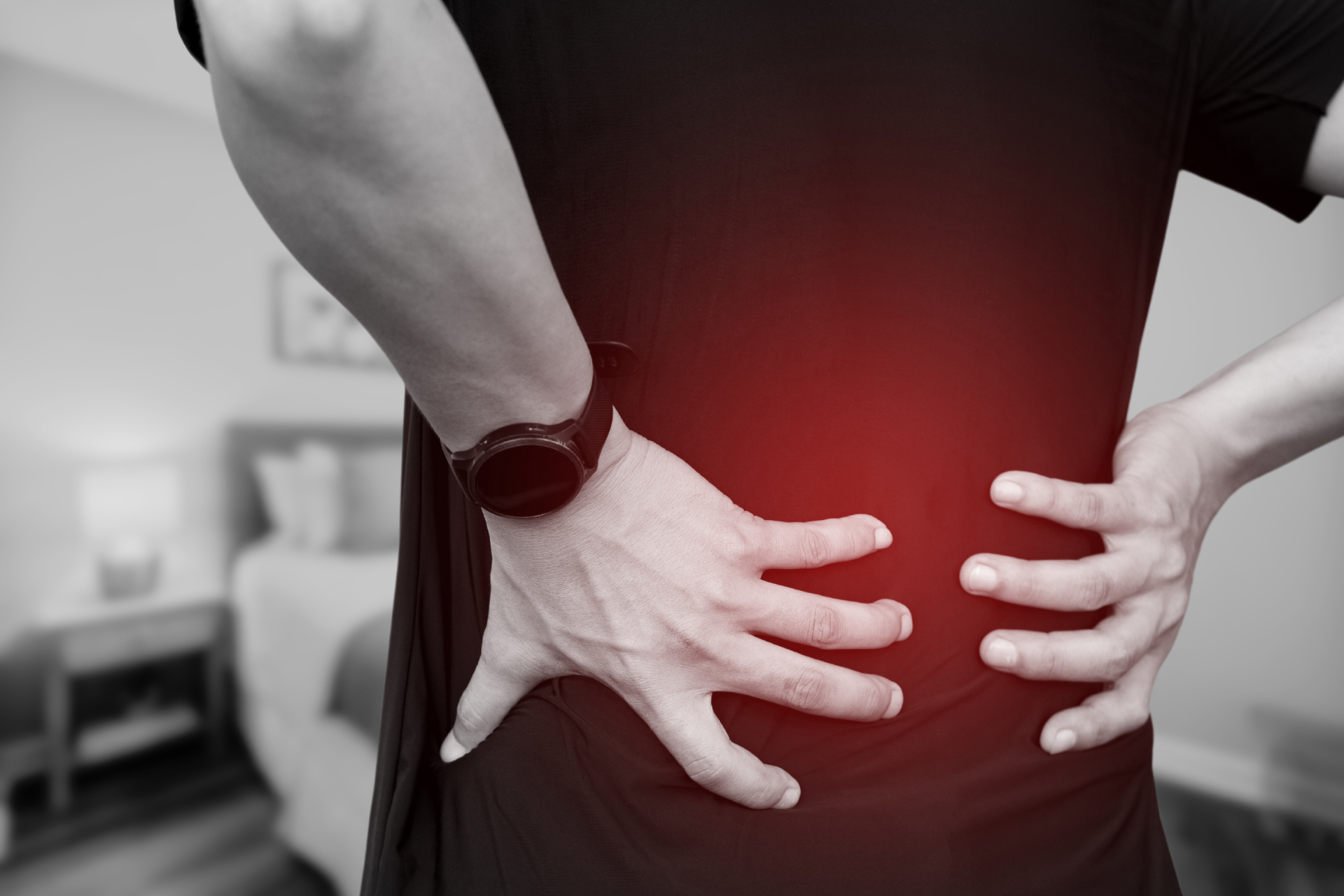 A black and white image of a man in black shirt holding his back due to chronic back pain.