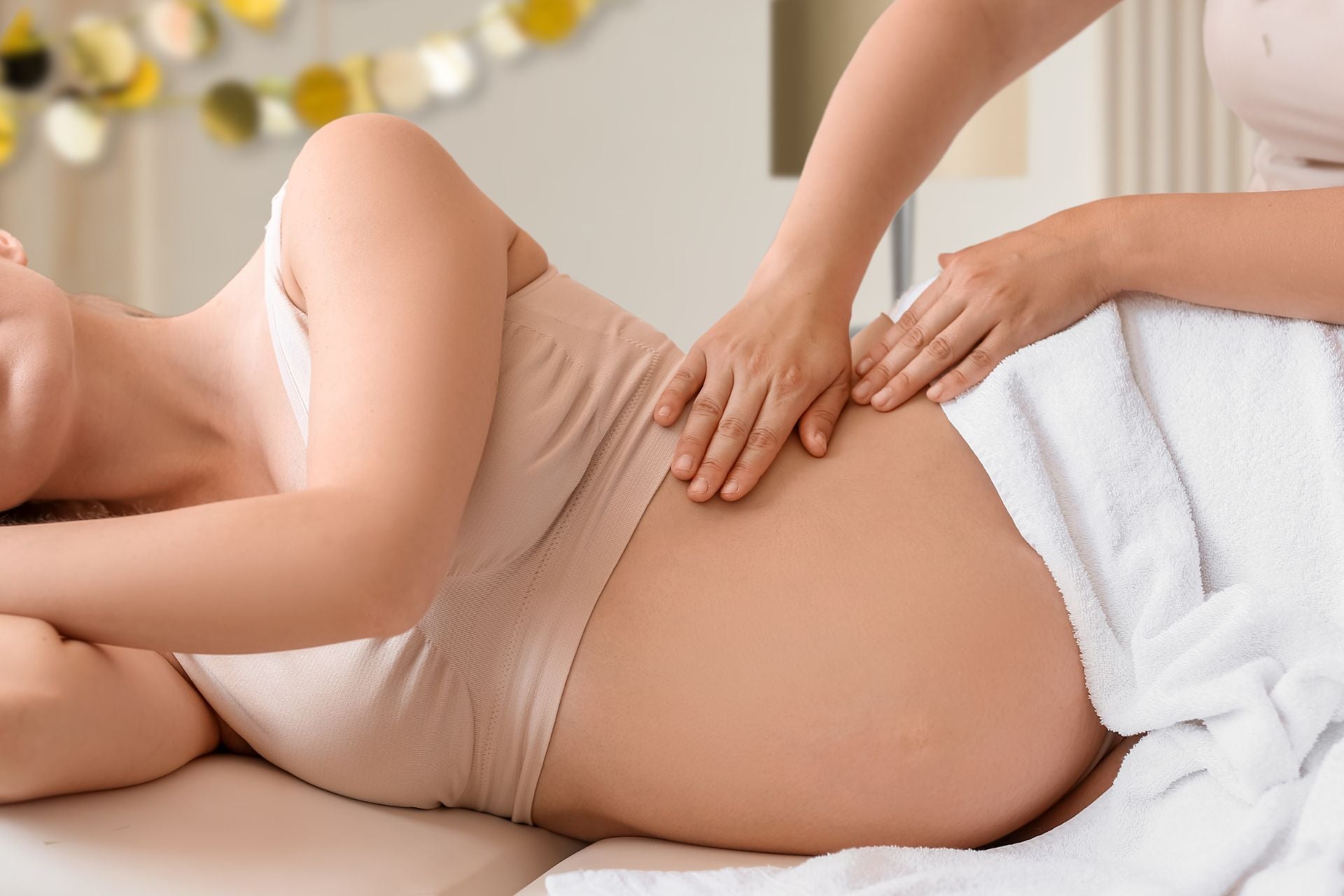 An image of a pregnant woman lying in bed with someone helping her manage pregnancy pain and swelling.