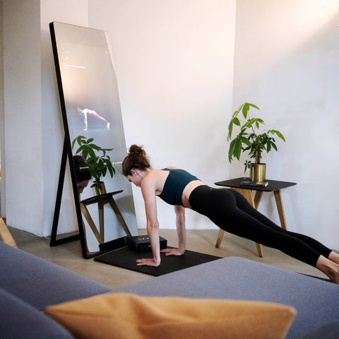 A woman doing a push up or a plank following the exercise shown on the VAHA X mirror