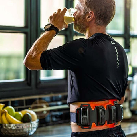 man drinking a glass of water and wearing a black FlexBeam in his lower back