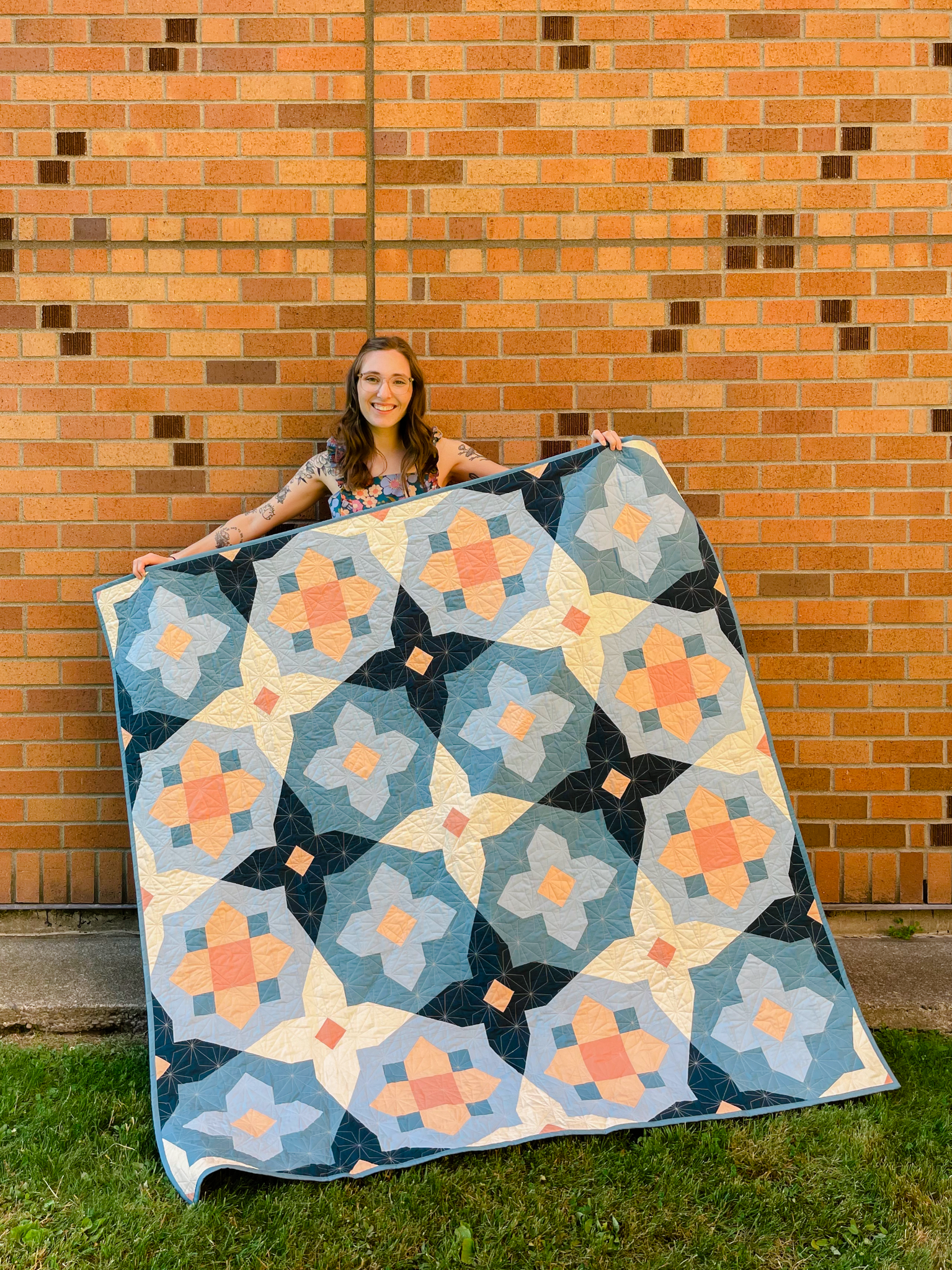 woman holding up blue, navy, peach and white quilt against brick wall