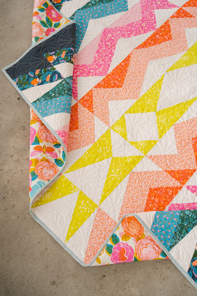 qulit laying on the ground with yellow , pink, orange and navy triangles radiating outward