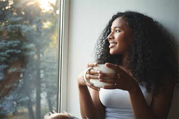 self-care-morning-routine-portrait-happy-charming-young-mixed-race-female-with-wavy-hair-enjoying-summer-view-through-window-drinking-good-coffee-sitting-windowsill-smiling-beautiful-daydreamer