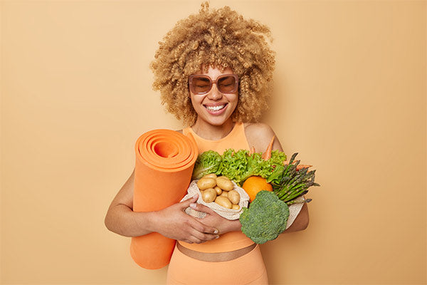 positive-woman-leads-healthy-sporty-lifestyle-poses-with-fitness-mat-different-fresh-vegetables-wears-sunglasses-casual-clothes-isolated-beige-background-proper-nutrition-concept