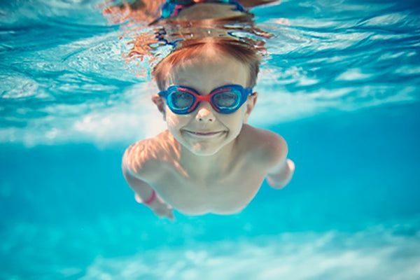 child swimming underwater with goggles and smiling