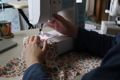 Rosie's hands and arms threading through the fabric into the sewing machine to create gathers