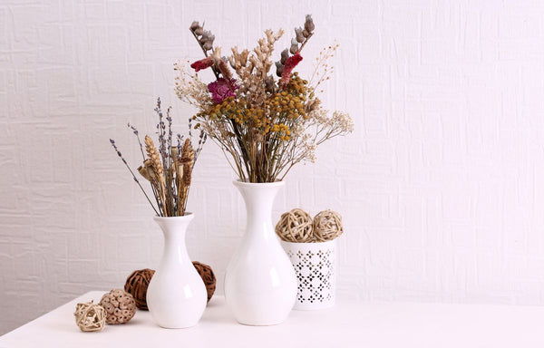 Two bouquets of dried flowers in a white vases