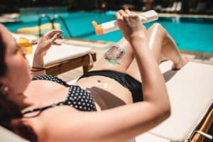 Modern woman applying sun cream for sun ray protection while relaxing at deck chair near pool side