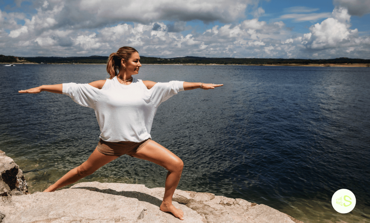 how your mental health impacts your motivation picture features Karena Dawn in Warrior Pose on a rock ledge in front of a lake