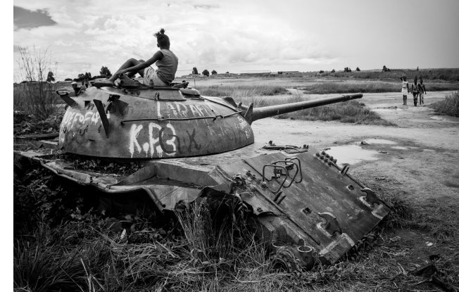 Alt: A young person sitting on an old tank in field, a remnant of conflict in Africa