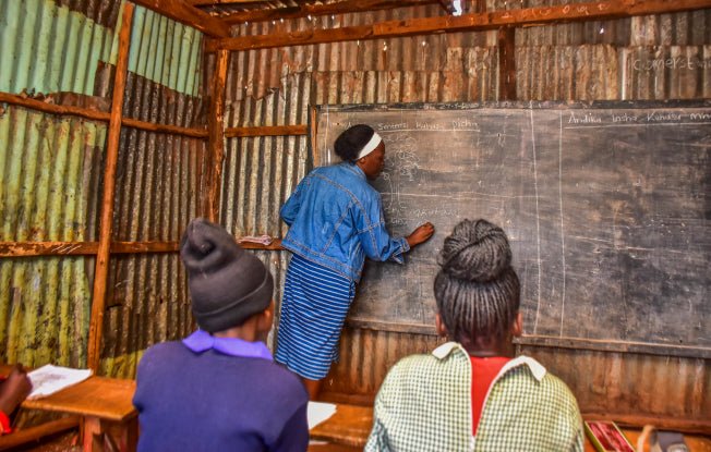 Alt: A teacher writes on the blackboard in a run-down school in Africa