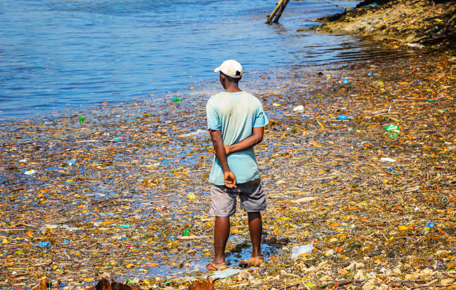 Alt: A young man stands ankle-deep in heavily polluted water