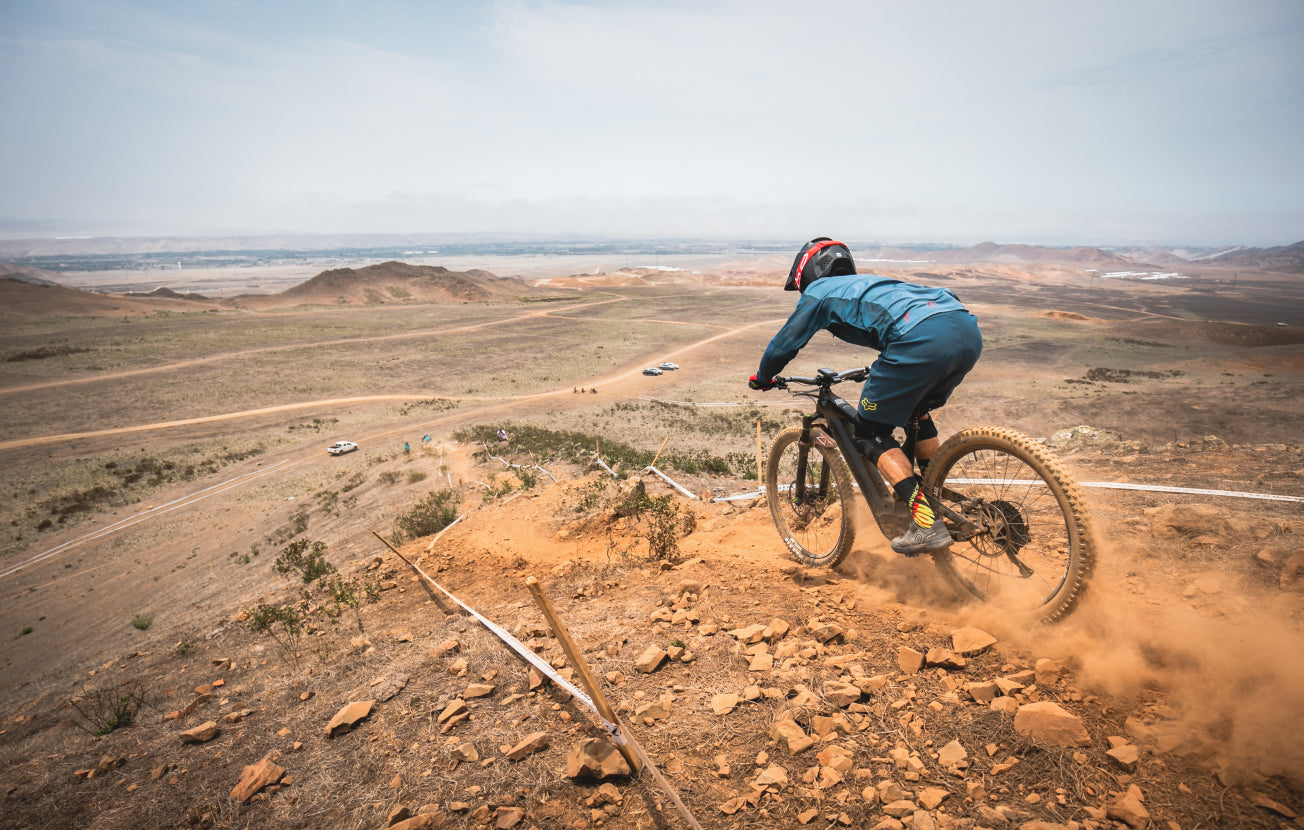 Alt: A mountain biker cycling down a dusty track on a vast, dry plain.