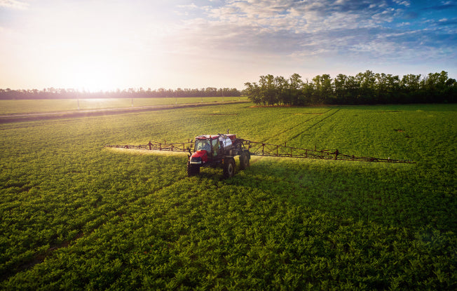 Alt: A red tractor spraying a field under a sunny sky