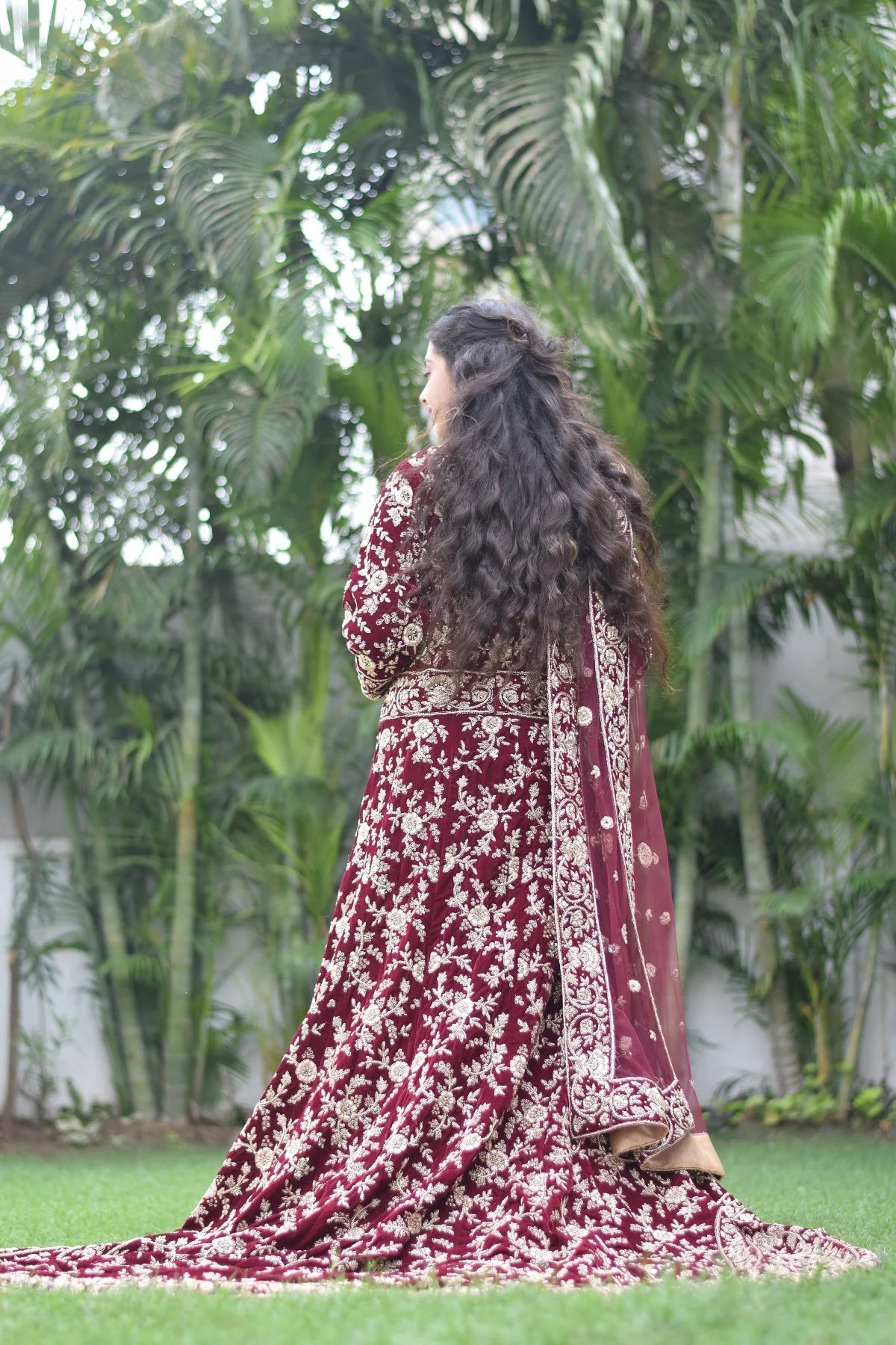 An Indian woman looks stunning in a maroon Trail Gown, complete with delicate embellishments and flowing fabric.