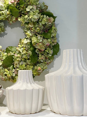 Faux hydrangea wreath on wall behind white vases
