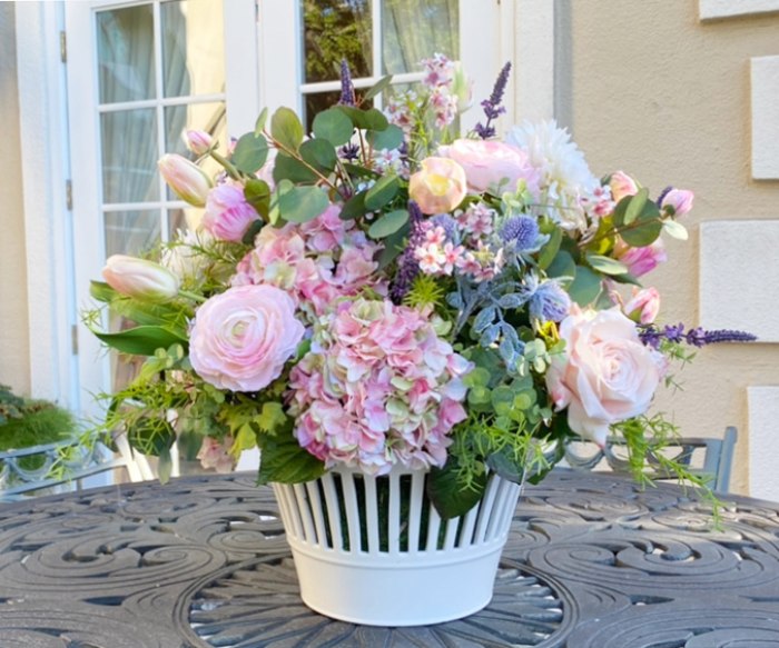 Realistic faux floral arrangement in a white ceramic vase on a metal patio table outdoors