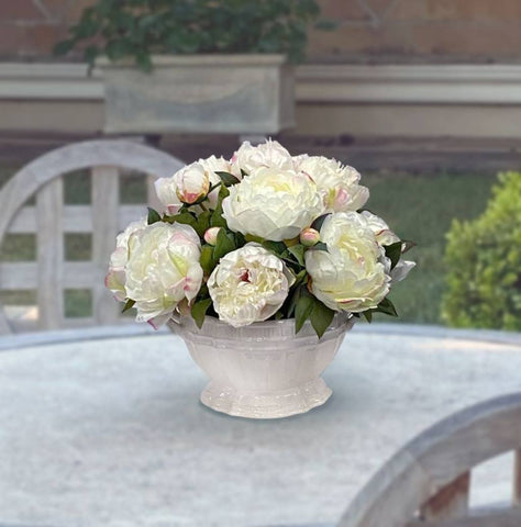 White artificial peonies in a ceramic planter on a table outside
