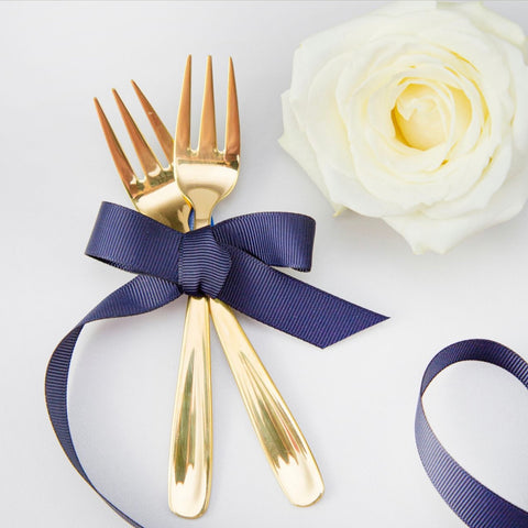 Gold forks, navy blue ribbon and a white rose