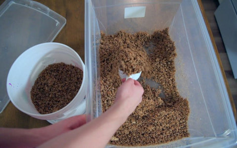 A person scoops a substrate from a container into a bucket.