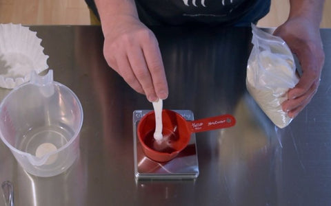 A person weights a gram of light malt extract on a scale.