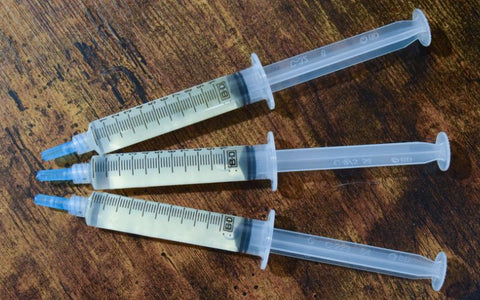 Three liquid culture syringes on a wooden desk.