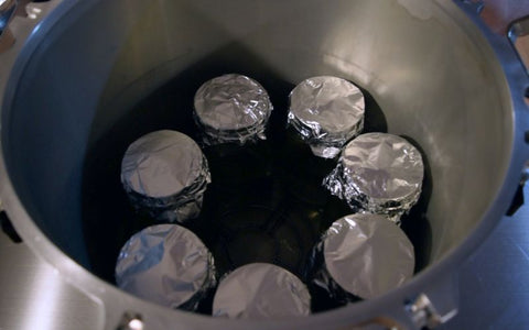Seven liquid culture jars packed into a pressure cooker. Each one is covered in foil.