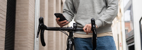 A cyclist walking beside his bike and using his phone with the Stride Charge Case on his phone