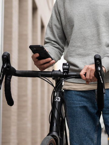 A cyclist walking beside his bike and using his phone with the Stride Charge Case on his phone