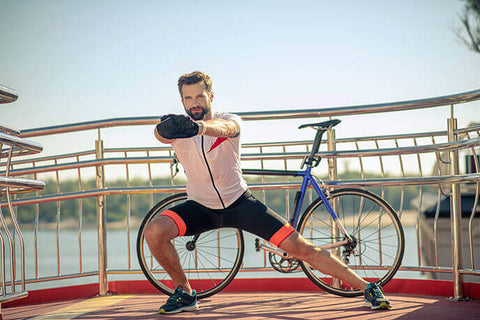 A man wearing cycling gear is stretching beside his bicycle while being outdoors