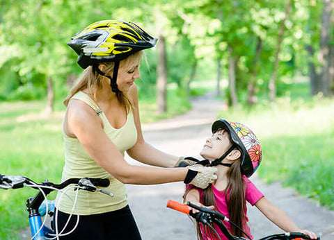 A mother putting a bike helmet on her daughter