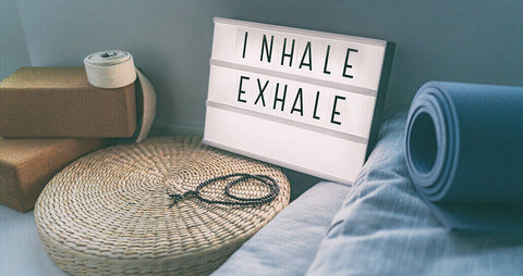 A sign that says 'Inhale, Exhale' with a yoga mat and yoga block beside it