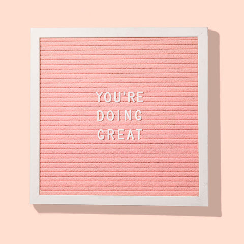 A pink letterboard in a white frame with the words 'You're doing great' in white capital letters, against a solid peachy pink background.
