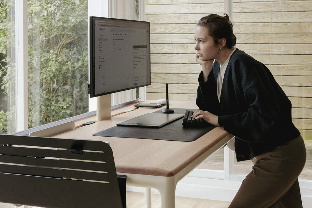 a woman stand in front of a standing desk and look at monitor