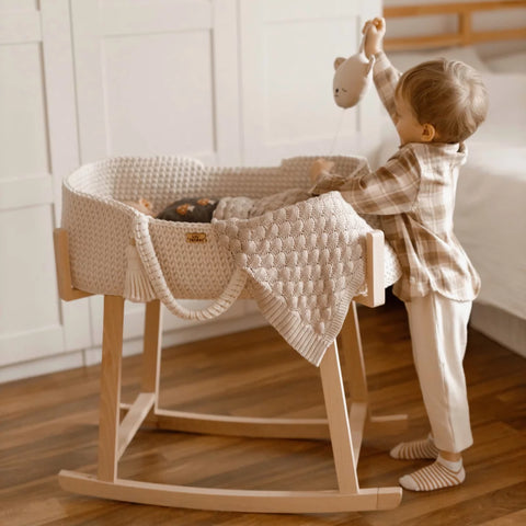 Crochet moses basket in a wooden stand and a boy standing next to it