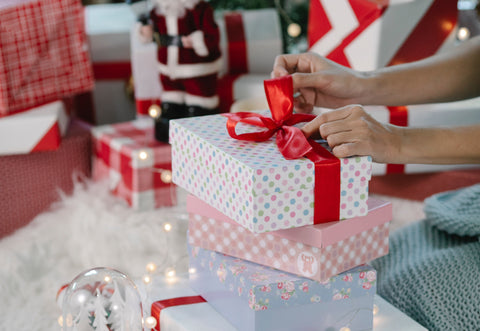 woman unwrapping wrapped gifts under christmas tree