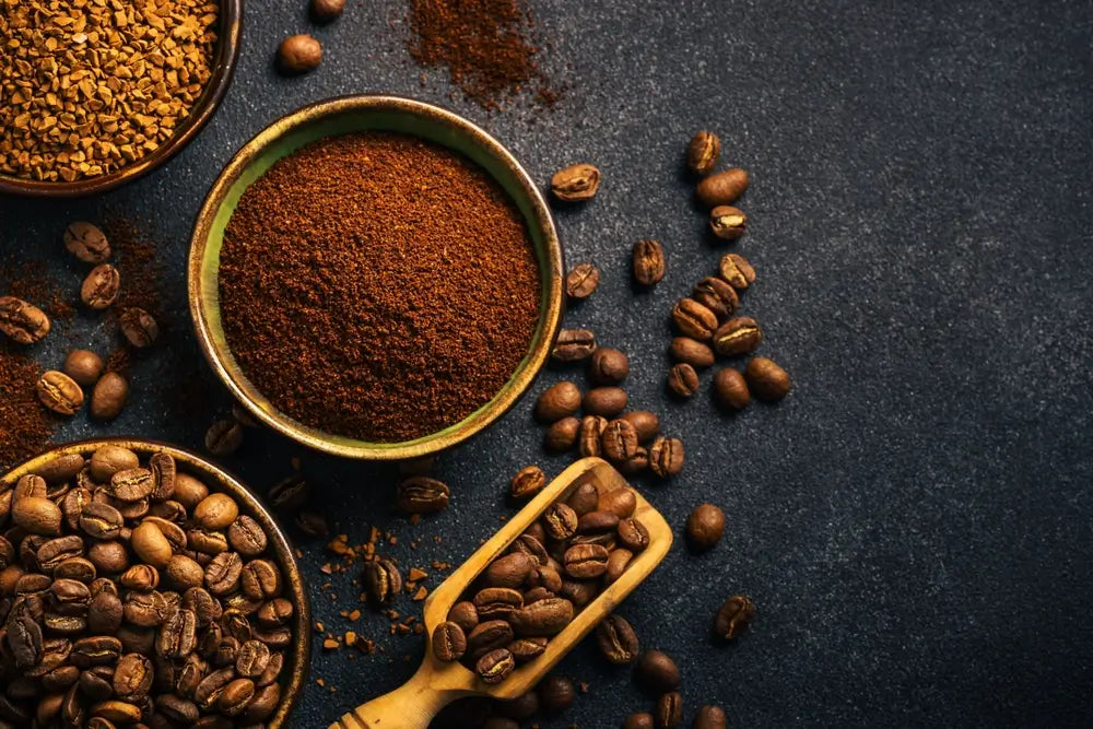 Roasted coffee beans, ground coffee and instant coffee in bowls at dark background.