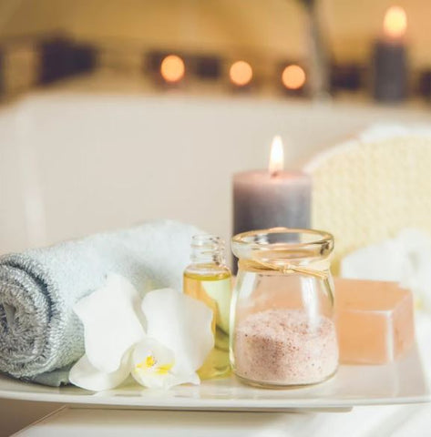 Photo of spa essentials at a bath tub including a scented candle, bath sales, and a rolled up towel